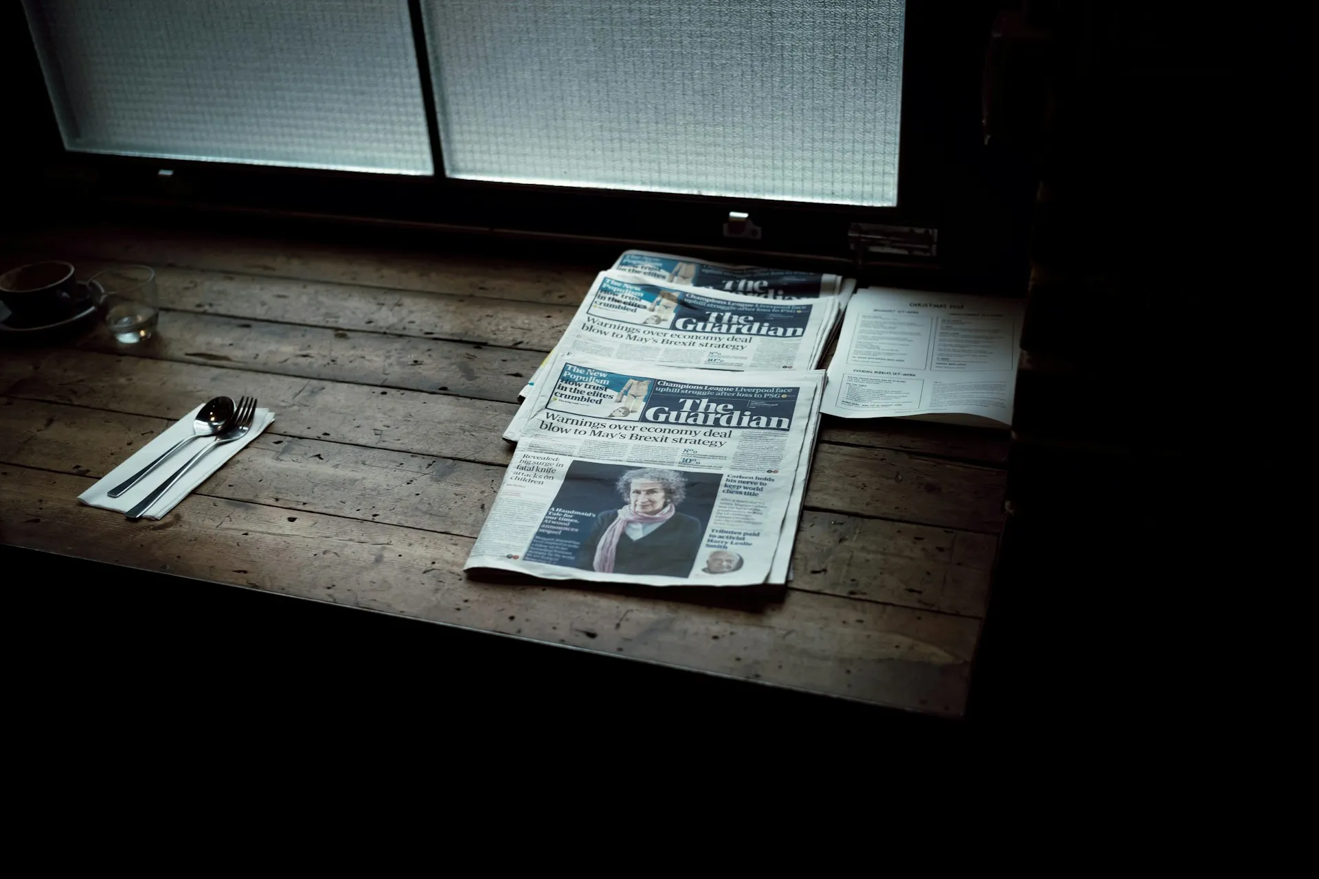Morning newspapers on a warm wooden table by a window
